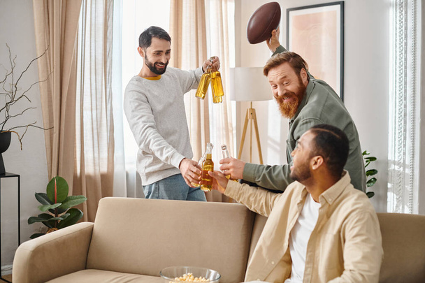 Два чоловіки, один тримає пляшку пива, сидять на затишному дивані, спілкуються і сміються у своєму повсякденному вбранні. - Фото, зображення