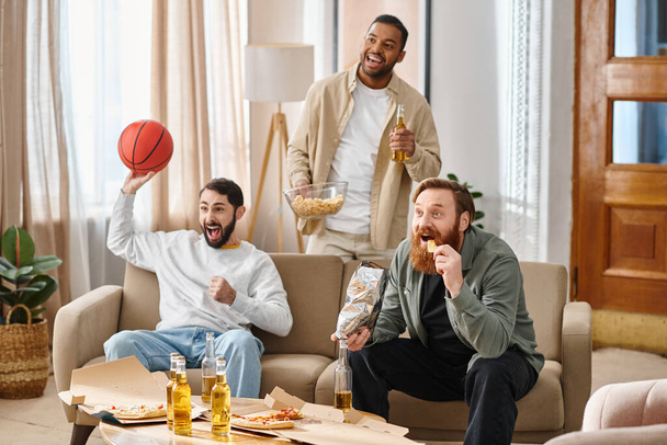 Two interracial handsome men in casual attire sitting on a couch, joyfully eating pizza and sipping beer, enjoying a fun night in together. - Photo, Image