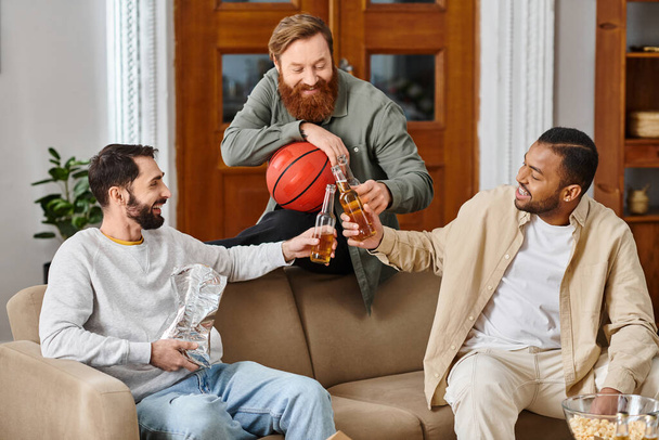 Trzech wesołych, przystojnych mężczyzn różnych ras siedzi blisko siebie na kanapie, ciesząc się chwilą przyjaźni i koleżeństwa.. - Zdjęcie, obraz