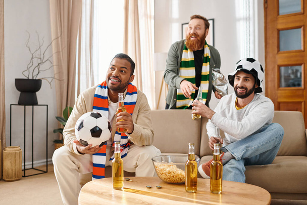 Drei gutaussehende, gut gelaunte Männer in lässiger Kleidung teilen Lachen und Geselligkeit in einer warmen, einladenden Wohnzimmeratmosphäre. - Foto, Bild