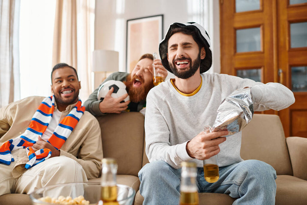 Tři pohlední, veselí muži různých ras, užívající si společnost na gauči v neformálním oblečení. - Fotografie, Obrázek
