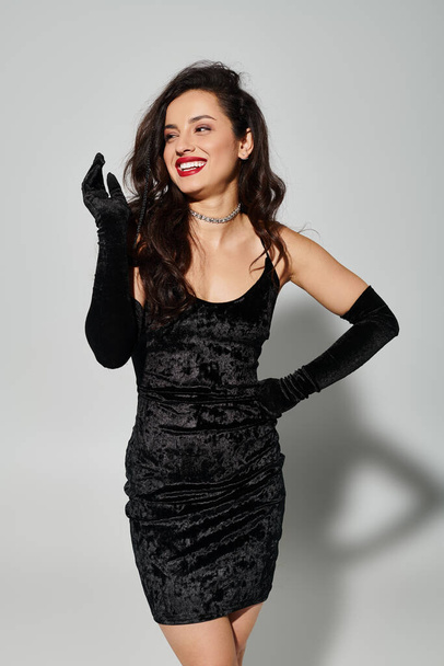 Una mujer con un vestido negro y guantes posando elegantemente en un ambiente elegante. - Foto, imagen