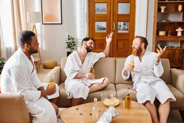 Три різноманітні, веселі чоловіки в халатах сидять на дивані, насолоджуючись компанією один одного у веселій і спокійній обстановці. - Фото, зображення
