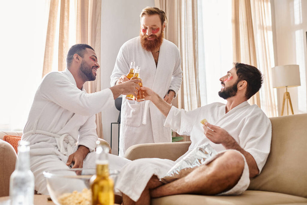 Kolme monipuolista miestä kylpytakit nauravat ja juttelevat viihtyisässä olohuoneessa. - Valokuva, kuva
