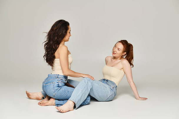 Дві елегантно одягнені жінки сидять на землі, зачаровані глибокою розмовою. - Фото, зображення