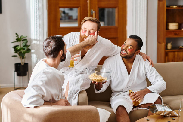 Tre uomini allegri in accappatoi godono di un momento accogliente in cima a un divano, mostrando l'essenza dell'amicizia e del cameratismo.. - Foto, immagini