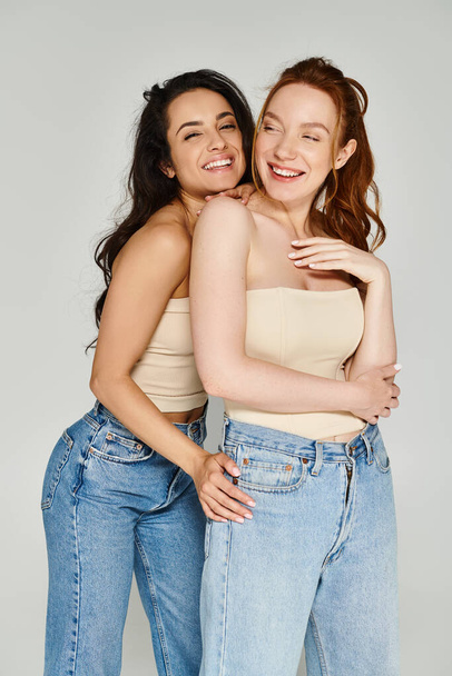 Δύο νεαρές γυναίκες με κομψή ενδυμασία αγκαλιάζονται σφιχτά, ακτινοβολούν με ευτυχία.. - Φωτογραφία, εικόνα
