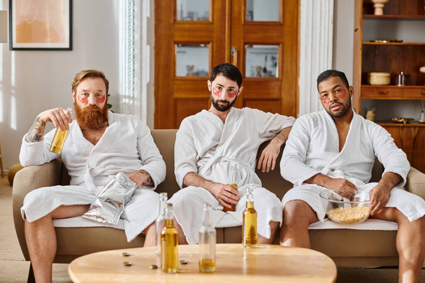 Three diverse, cheerful men wearing bathrobes, sitting on top of a couch, enjoying a great time together. - Photo, Image