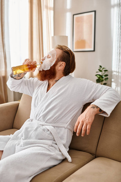 Un hombre con atuendo casual se sienta cómodamente en un sofá, sorbiendo tranquilamente una cerveza. - Foto, imagen