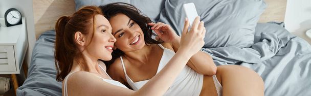 Deux femmes joyeuses, élégamment vêtues, blotties sur un lit dans une étreinte aimante. - Photo, image