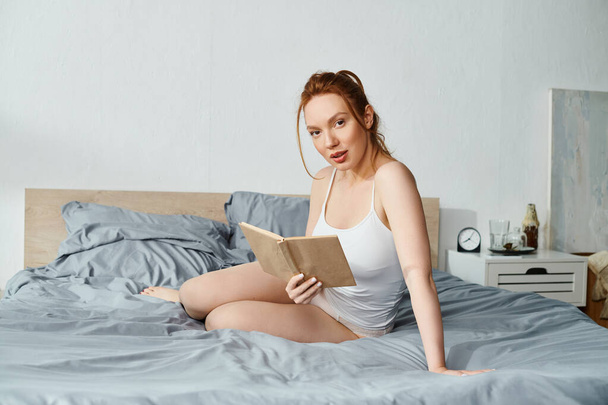 Uma mulher em traje elegante lê pacificamente um livro enquanto se senta em uma cama. - Foto, Imagem