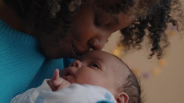 Μέση closeup με αργό ρυθμό της νεαρής στοργικής μητέρας φιλιά μέτωπο του νεογέννητου γιου της, ενώ λικνίζεται στο σπίτι το απόγευμα - Πλάνα, βίντεο