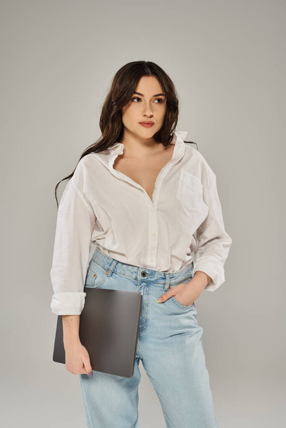A beautiful plus-size woman in a white shirt and jeans holding a folder on a grey backdrop. - Photo, Image