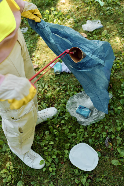 Αφροαμερικάνος καθαρίζει πάρκο και κρατάει μπλε τσάντα δίπλα στη γυναίκα του. - Φωτογραφία, εικόνα