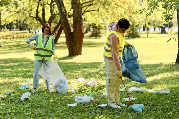 Een divers, liefdevol koppel met veiligheidsvesten en handschoenen in het gras, dat het park met zorg en eenheid schoonmaakt. - Foto, afbeelding
