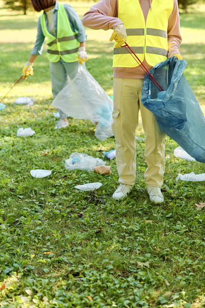 Een sociaal actief en liefdevol koppel, met veiligheidsvesten en handschoenen aan, staan samen in het gras het park schoon te maken. - Foto, afbeelding