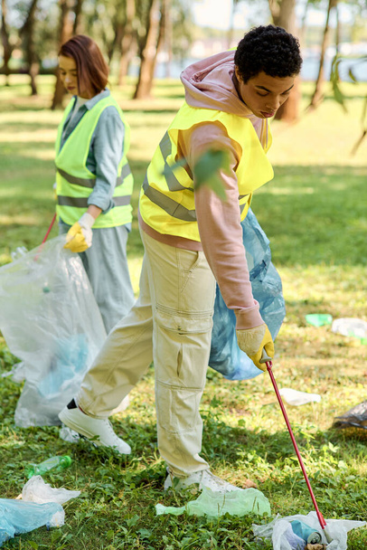 A socially active, diverse loving couple in safety vests and gloves cleaning a lush green park together. - Photo, Image