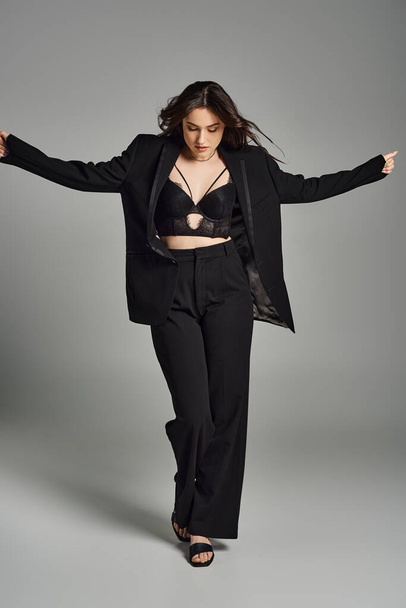 A beautiful plus-size woman in a stylish black suit dances gracefully against a gray backdrop. - Photo, Image