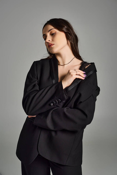 Elegante mujer de talla grande en un traje negro posa con confianza sobre un fondo gris, exudando elegancia y gracia. - Foto, Imagen