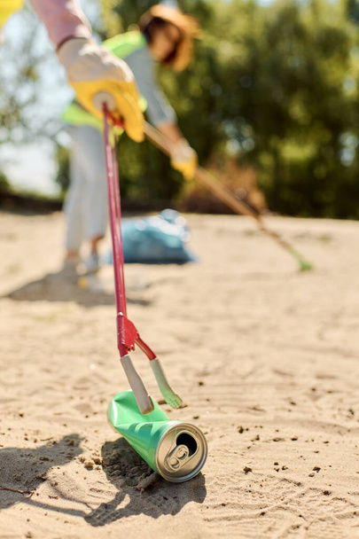 Nainen turvaliivissä ja hanskat ahkerasti puhdistaa hiekkaa puistossa, kun hänen kumppaninsa auttaa, osoittaen omistautumista puhtaus. - Valokuva, kuva