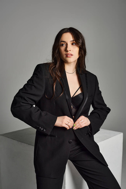 A beautiful plus size woman strikes a confident pose in a stylish black suit against a grey backdrop. - Photo, Image