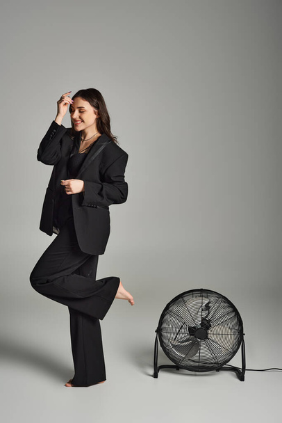 Een mooie plus size vrouw in stijlvolle kledij, staat sierlijk voor een ventilator, haar outfit fladdert in de wind. - Foto, afbeelding