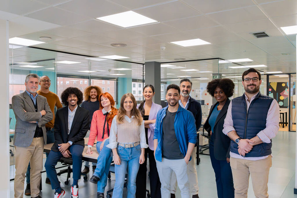 Een gevarieerde groep professionals die glimlachen en samen poseren in een hedendaagse coworking kantoorruimte.  - Foto, afbeelding