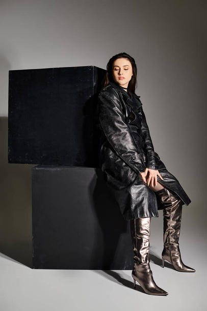 Een extra grote vrouw in stijlvolle kleding zit sierlijk bovenop een zwarte doos tegen een grijze achtergrond. - Foto, afbeelding