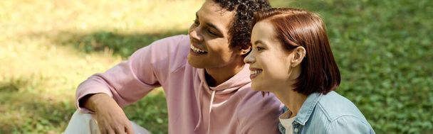 Um casal amoroso em trajes vibrantes se senta perto um do outro em um parque, irradiando felicidade e conexão. - Foto, Imagem