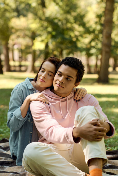Una coppia eterogenea, vestita in modo vivace, seduta su una coperta nel parco, che si gode un momento di pace insieme. - Foto, immagini