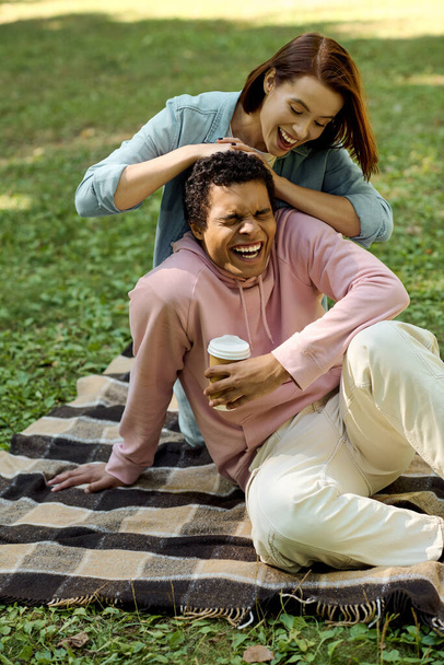 Zróżnicowana, kochająca się para siedząca na kolorowym kocu w parku, dzieląca ze sobą intymne chwile. - Zdjęcie, obraz
