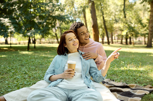 Una pareja vibrante y diversa en traje colorido se sienta en una manta en el parque, disfrutando de un momento sereno juntos. - Foto, Imagen