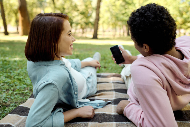 Couple aimant divers, vêtu de façon vibrante, assis joyeusement sur une couverture dans un cadre de parc. - Photo, image