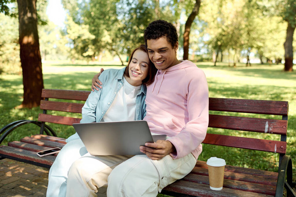 Una pareja en traje vibrante se sienta junta en un banco del parque, absorta en la pantalla de un ordenador portátil, disfrutando de la compañía de los demás. - Foto, imagen