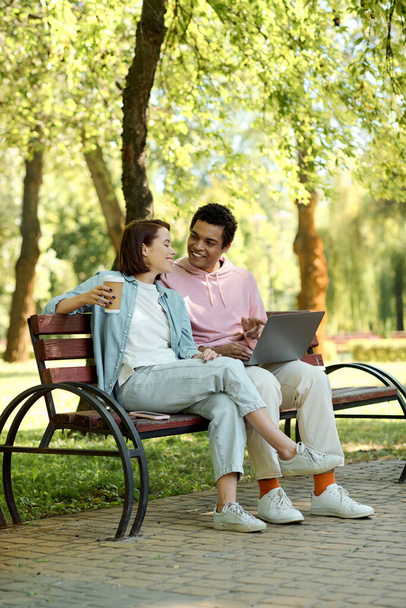 Een stijlvol gekleed echtpaar, ondergedompeld in de digitale wereld, zit op een bankje in het park, verzonken in het scherm van een laptop. - Foto, afbeelding