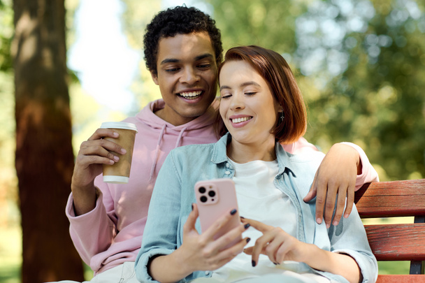 Un couple diversifié en tenue vibrante est assis sur un banc, absorbé dans un téléphone portable ensemble. - Photo, image