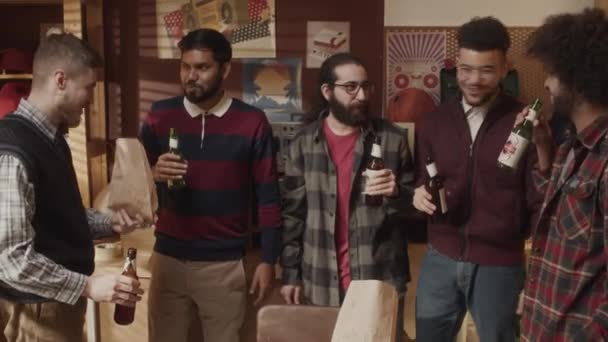 民族的に多様な男性ギークのチームのドリーアウトショット ビールのボトルを凝視し,ハイテクスタートアップの成功を祝う古風なアパートで一緒に取得しながらチャット - 映像、動画