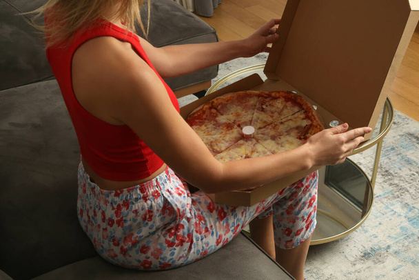 Nő eszik elvitelre pizza dobozból, miközben otthon pihen a kanapén - Fotó, kép