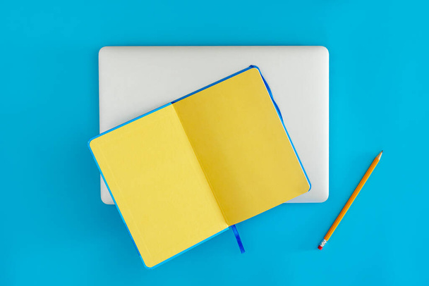 Otwórz żółty notatnik i laptop na niebieskim tle, widok z góry. Koncepcja planowania, pracy i edukacji. Przestrzeń kopiowania. - Zdjęcie, obraz