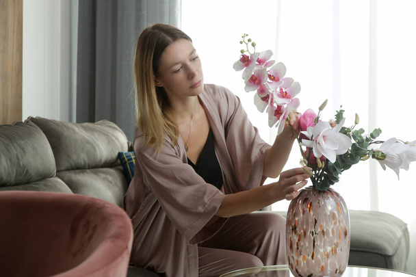Woman arranging vase with flowers. Housewife taking care of coziness in apartment. Interior decor, household and home improvement concept. - Photo, Image