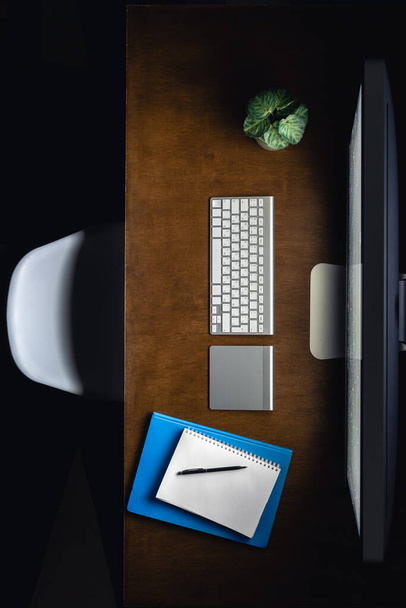Компьютер, блокноты и чашка чая на рабочем столе ночью, вид сверху. Рабочее место в офисе поздно ночью. Концепция работы ночью. - Фото, изображение