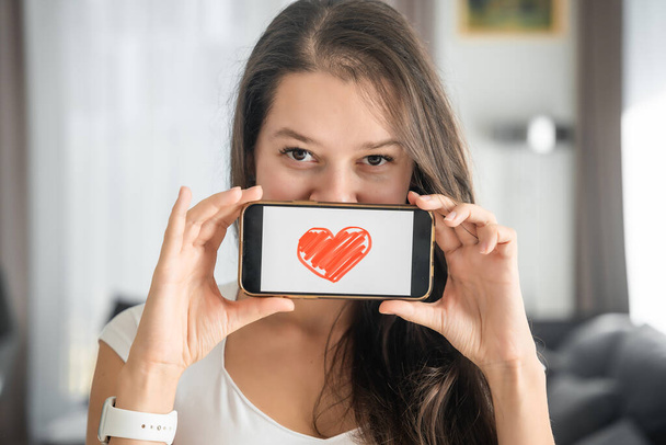 Dünya Sağlık Günü konsepti. Akıllı telefonunda kalp örnekleri gösteren genç bir kadın, kardiyovasküler sağlık bilincinin uluslararası sağlık gözlemi üzerindeki önemini gösteriyor..  - Fotoğraf, Görsel