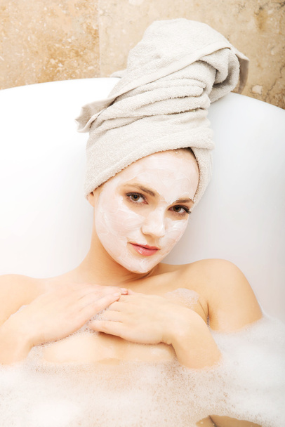 Woman relaxing in bathtub with face mask. - 写真・画像