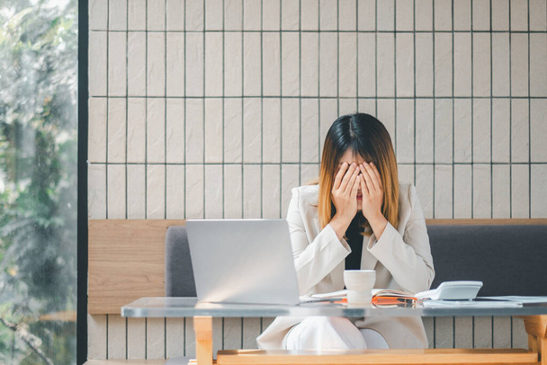 Empresaria abrumada cubriéndose la cara con las manos, mostrando estrés mientras trabaja en su computadora portátil en un café - Foto, imagen