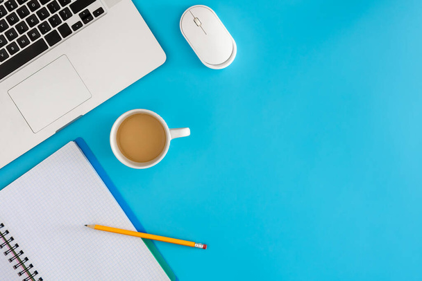 Büroarbeitsplatzkonzept. Laptop mit Notizbuch und Tasse Kaffee auf blauem Hintergrund. Draufsicht mit Kopierraum, flache Lage. - Foto, Bild
