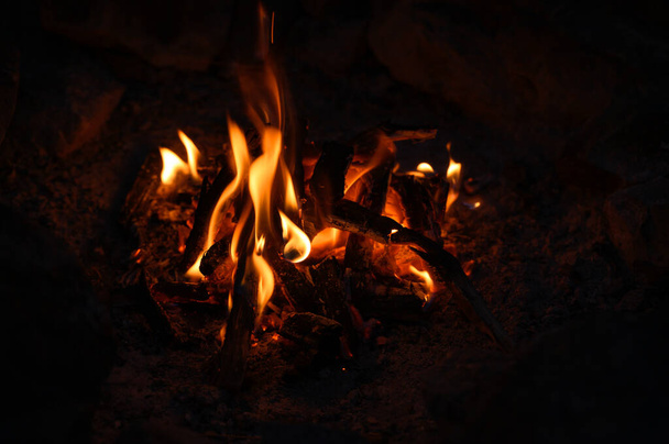 Костер в туристическом лагере. Горящее дерево. Пламя и огонь искрятся на темном фоне - Фото, изображение