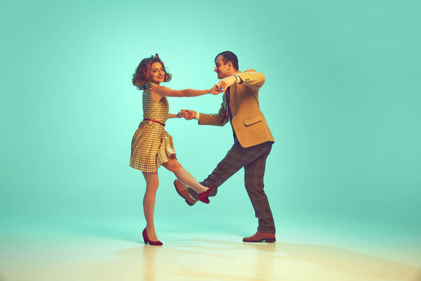 Retrato dinámico de pareja atractiva en atuendo retro bailando boogie-woogie contra fondo de menta degradado. Concepto de música y danza, hobby, energía, felicidad, humor, acción, vintage - Foto, imagen