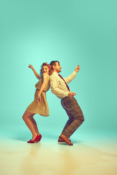 Hombre y mujer alegres y positivos en la clásica moda de los años 50 bailando enérgicamente contra el gradiente fondo de menta. Concepto de arte, amor, música, energía, felicidad, humor del viernes, acción, belleza y moda. - Foto, imagen