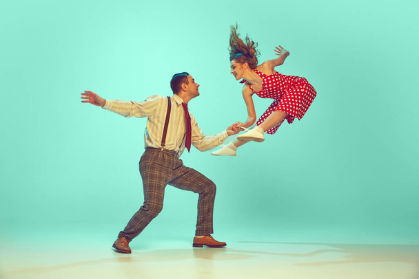 Captura dinámica de la escena de baile swing enérgico, pareja actuando en movimiento contra el fondo de la menta gradiente. Moda retro. Concepto de jazz, comparaciones de épocas, música, energía, felicidad, humor, acción - Foto, imagen