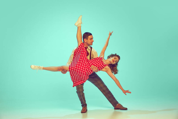 Swing dansers stralen geluk terwijl het uitvoeren van energetische dans beweegt in beweging tegen gradiënt munt achtergrond. Concept van muziek, hobby, kunst, energie, geluk, stemming, actie, jaren 60, jaren 70 cultuur - Foto, afbeelding